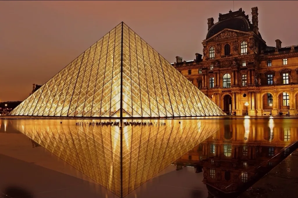 Pyramide du Louvre illuminée à la tombée du jour, reflétée dans le bassin, avec l'aile Renaissance du palais en arrière-plan