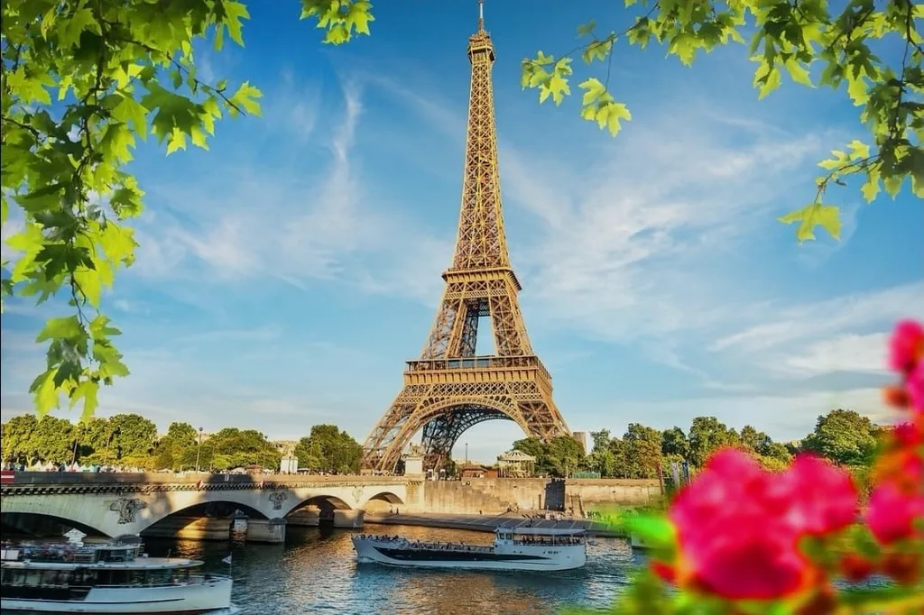 Tour Eiffel entière vue depuis les quais de Seine en été, un bateau-mouche passant sous le pont d'Iéna, feuillages verts en cadre