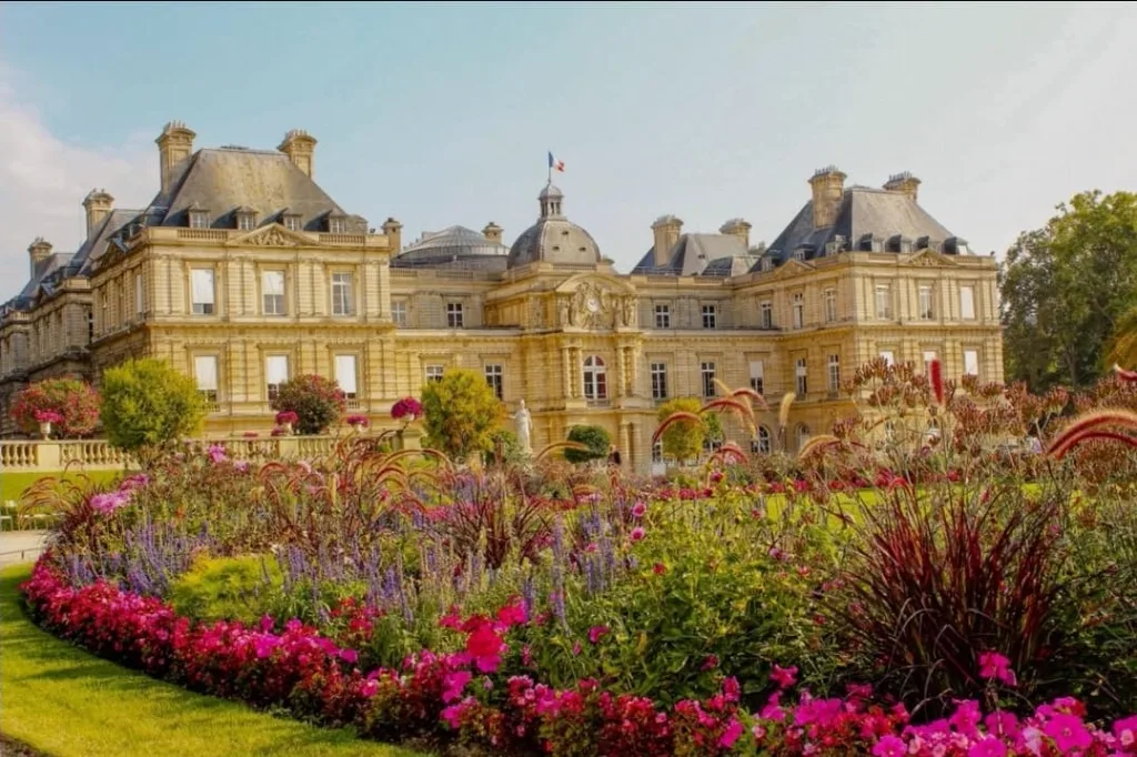 Palais du Luxembourg derrière un massif de fleurs roses et pourpres en pleine floraison sous un ciel clair